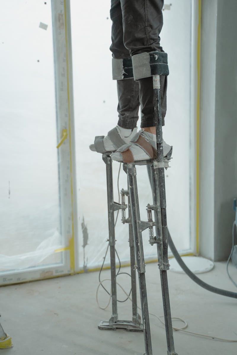 Worker on stilts adjusting high areas in a room under renovation.