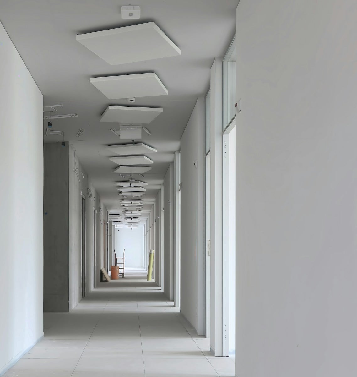 a long hallway with white walls and ceiling lights A large room with a lot of white paint on the walls Best Drywall Guide: Learn All About Drywalling